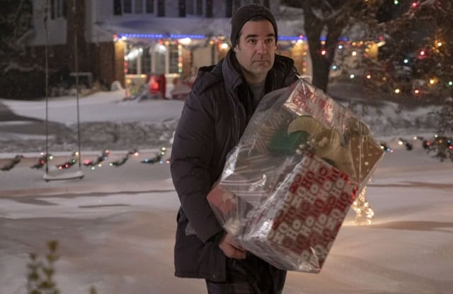 Man holding a bag of Christmas presents outside in the snow.