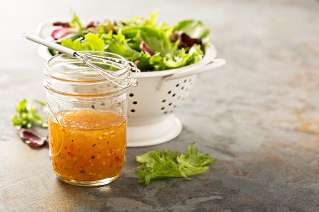 collander with lettuce and a mason jar with salad dressing