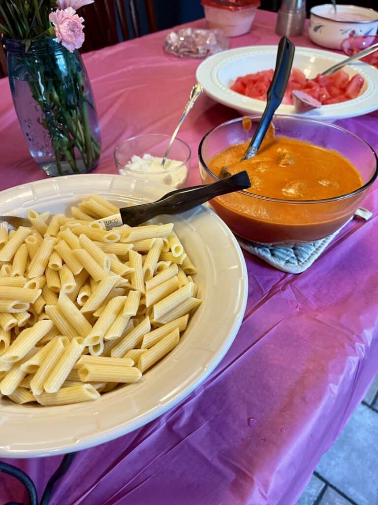 Bowl of penne pasta next to a bowl of pink pasta sauce.