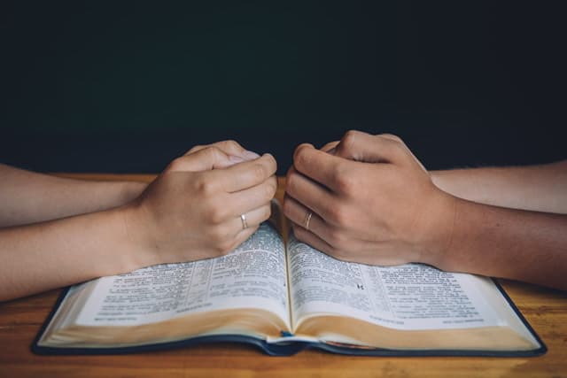 couple hands praying over bible