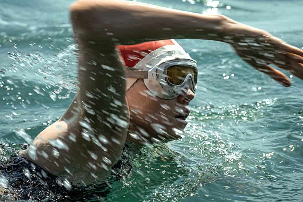 Woman swimming. She is wearing an orange swimming cap and white swim googles