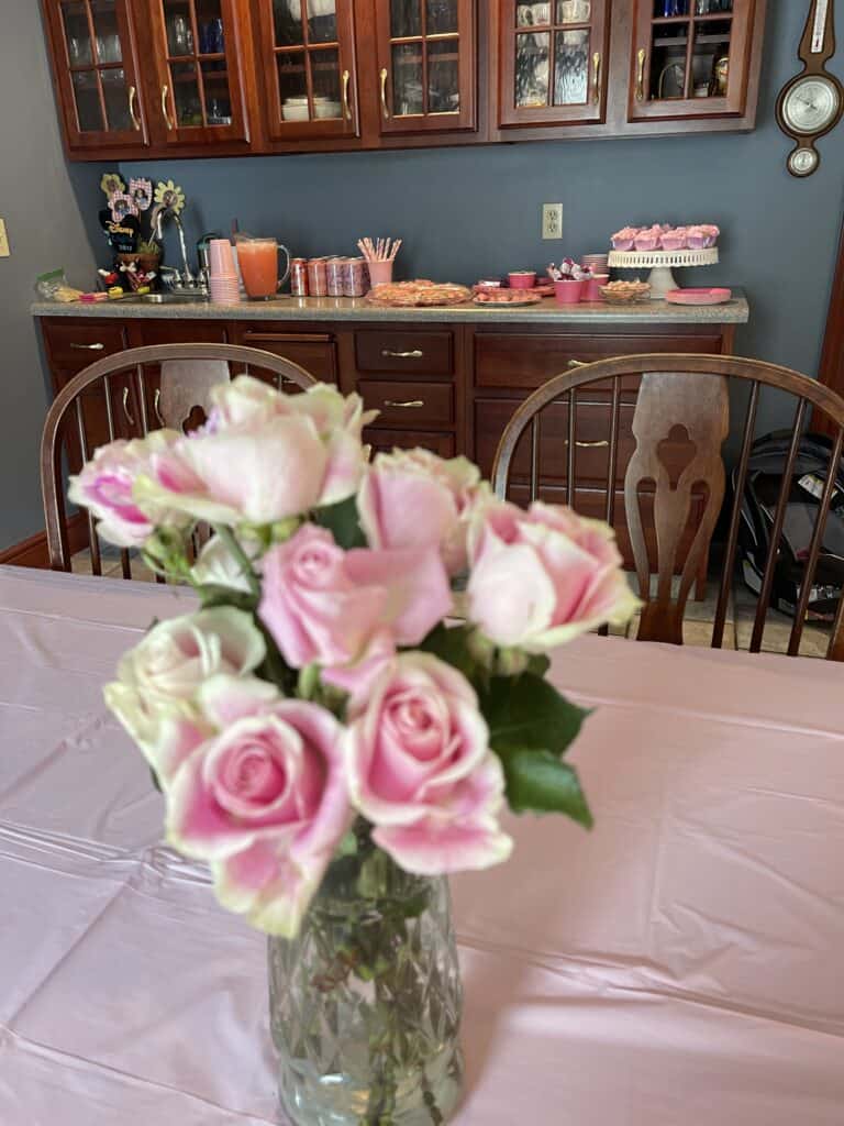 Pink tablecloth with pink roses and pink dessert bar in the background.