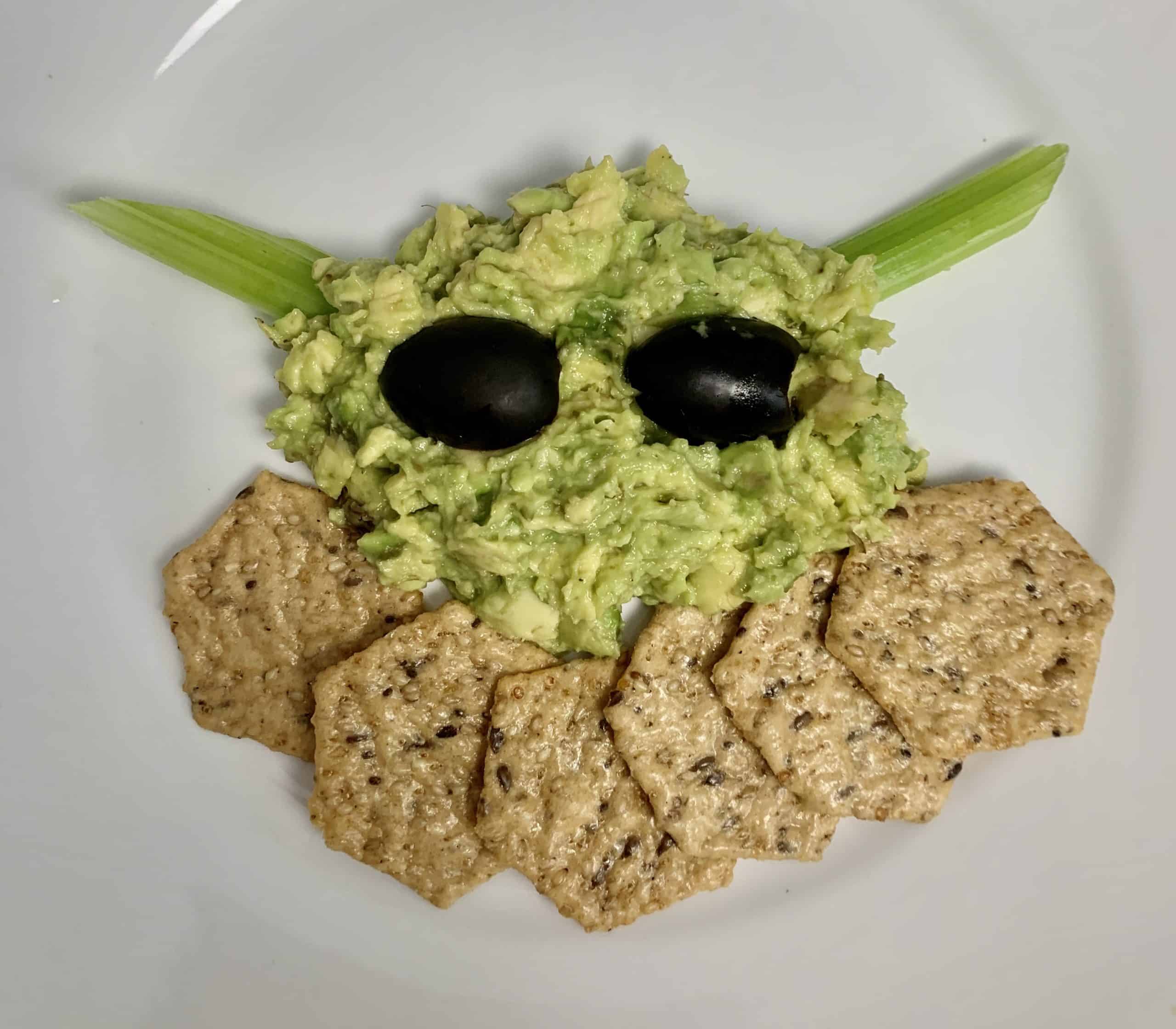 Avocado celery crackers and black olives form Baby Yoda face