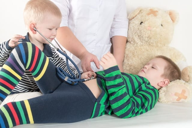 Little white boy with stethoscope listening to his older brothers “stomach” noises.