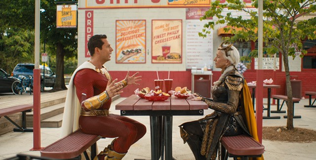 Superhero Shazam and older woman Greek mythology sitting at picnic bench with food in front of them