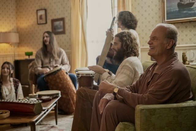 People sitting in a family room including older gentleman and hippie youth.
