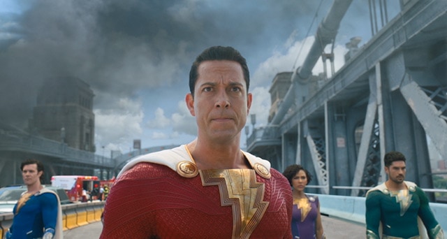Zachary Levi as Shazam standing on a bridge with a cloud of dark smoke behind him.