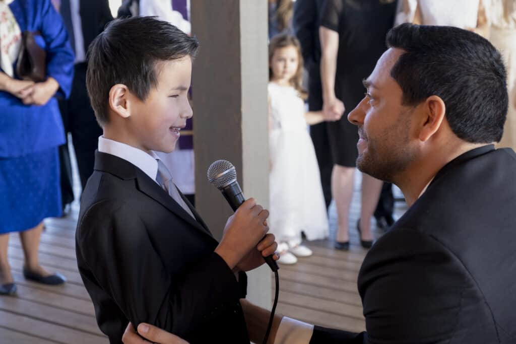 Zachary Levi dressed in suit listening to a boy sing with a microphone