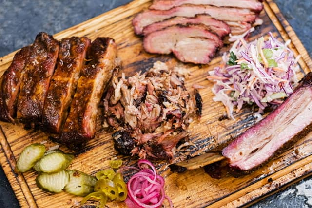 Beef brisket, pickles, picked onion, and cole slaw sitting on a wooden cutting board