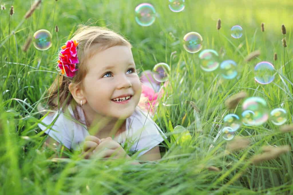 Toddler girl laying in tall grass with soap bubbles aound her
