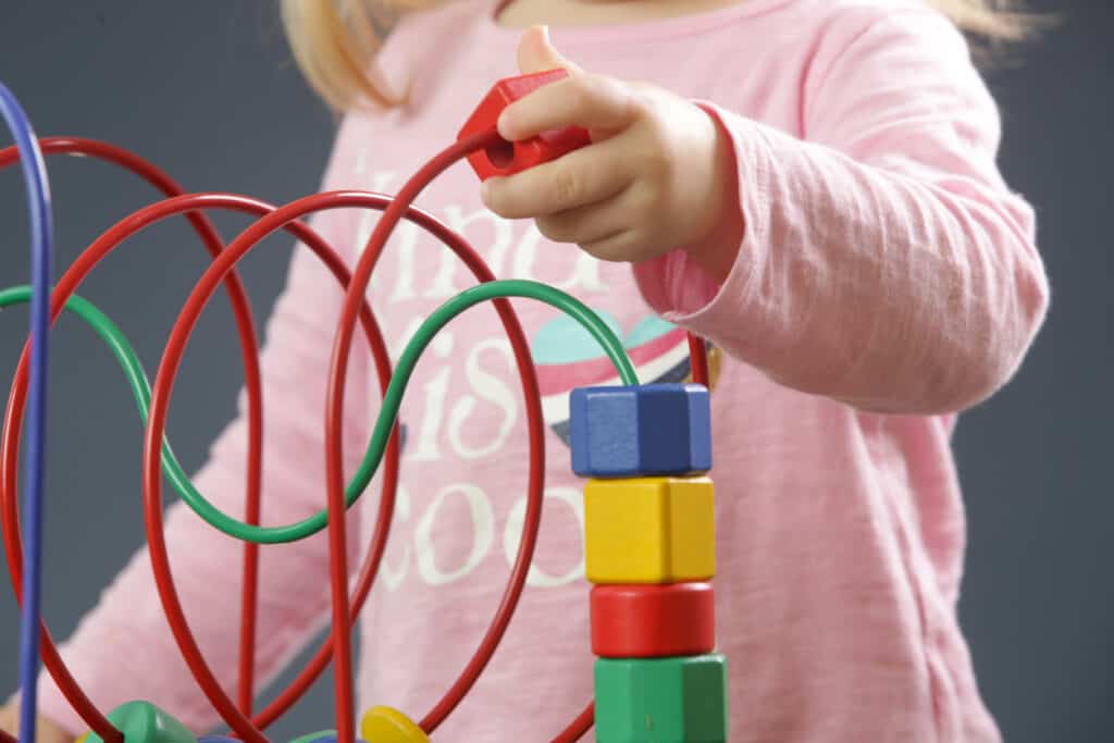 Toddler girl playing with a wire and block toy