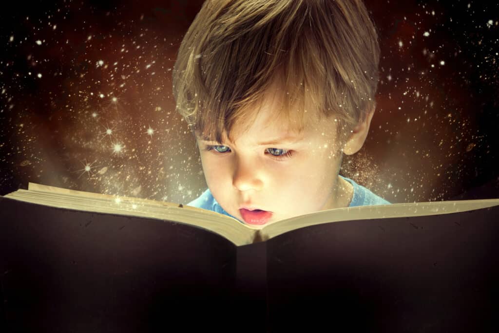 Little boy looking at a book in wonder with stars around him.
