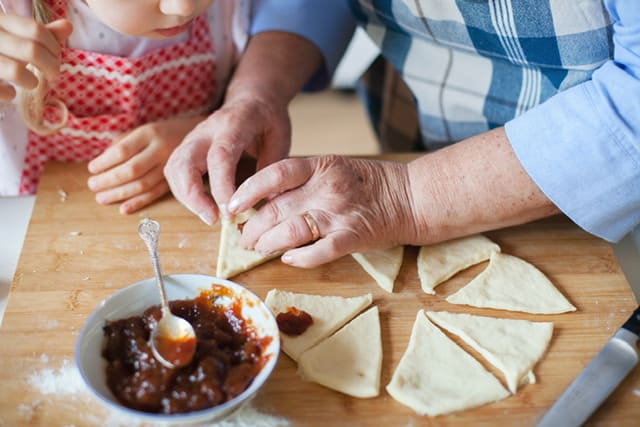 hands of an elderly women making cookies with young child watching