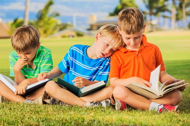 3 boys reading outside in the grass