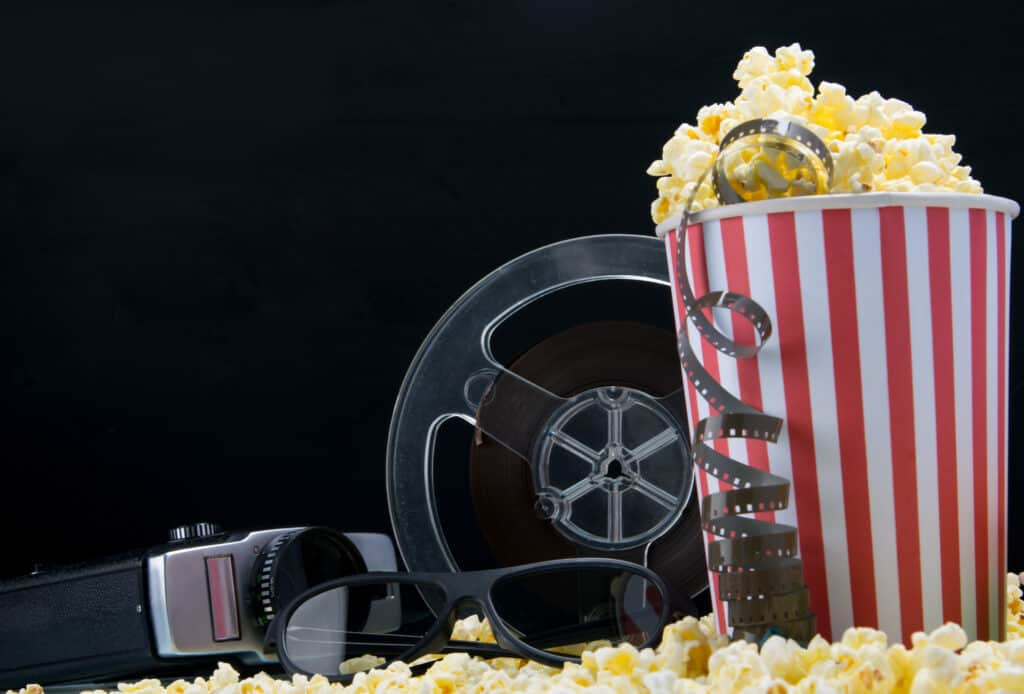 Movie camera, movie film reel, black glasses, red and white striped popcorn bucket and popcorn