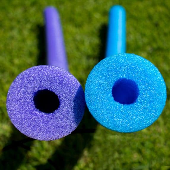 Two pool noodles, one is purple and one is blue.
