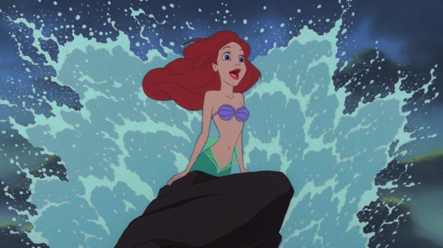 The animated Little Mermaid Ariel splashing up from the sea with water around her and holding onto a rock.
