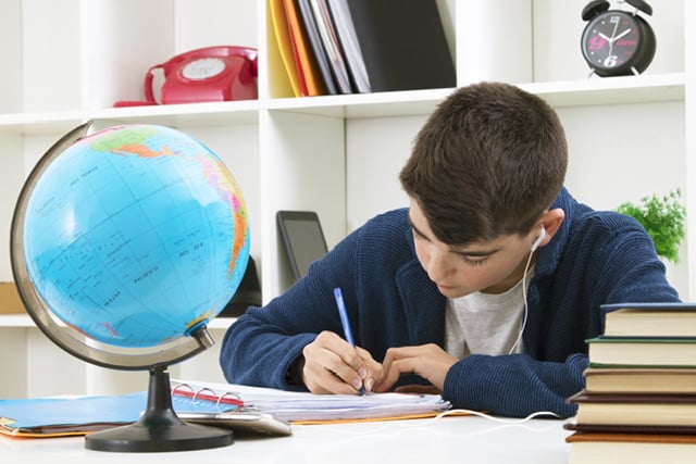 boy writing at a desk. There is a world globe on the desk.