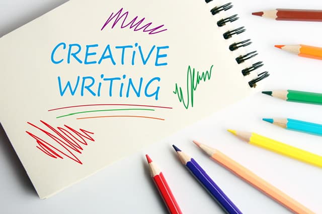 The word Creative Writing on a notebook in color with colored pencils around the notebook