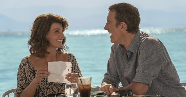 Woman and a man sitting near the beach talking and laughing.