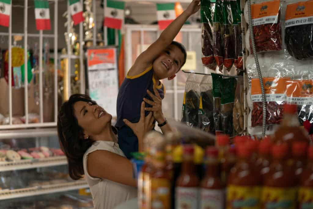 A woman holds a young boy up to get some chili peppers in a convenience store.