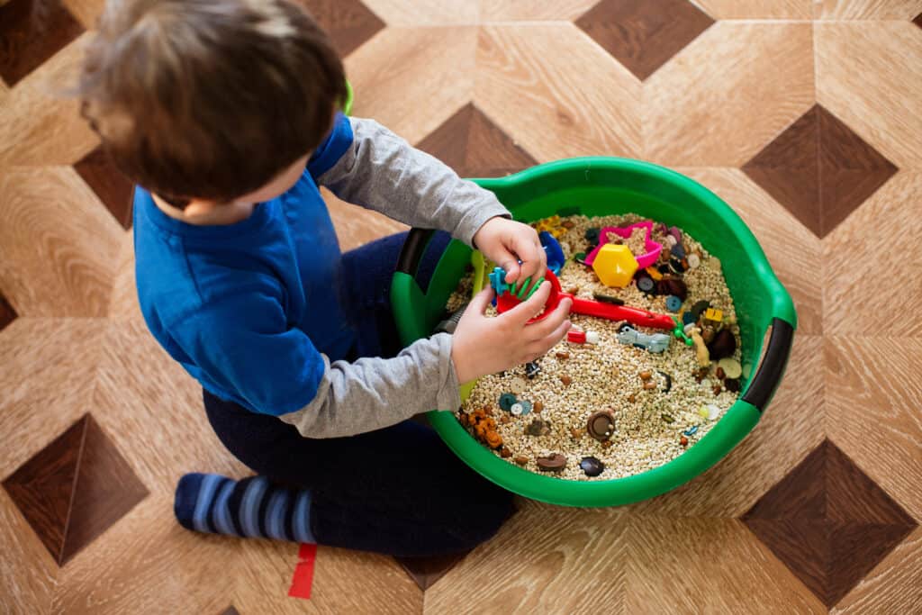 young boy playing with a sensory bin filled with toys.