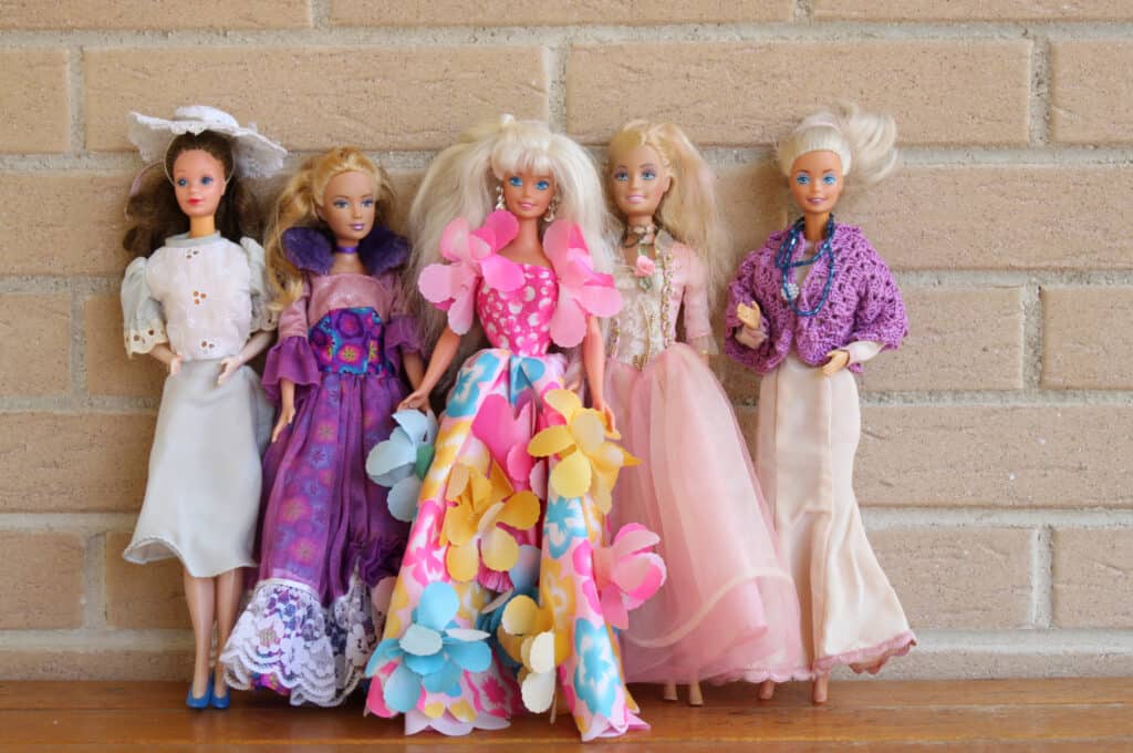 5 Barbie dolls lined up against a brick wall
