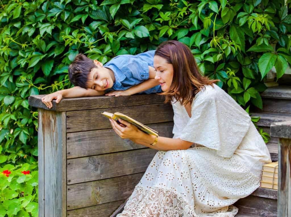 Mom reading book to son. They are sitting outside.