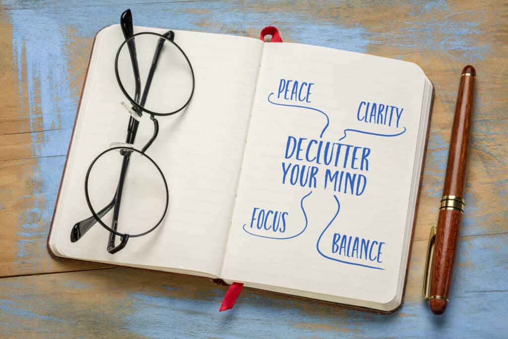Declutter Your Mind written in a notebook with glasses and a pen sitting on a desk