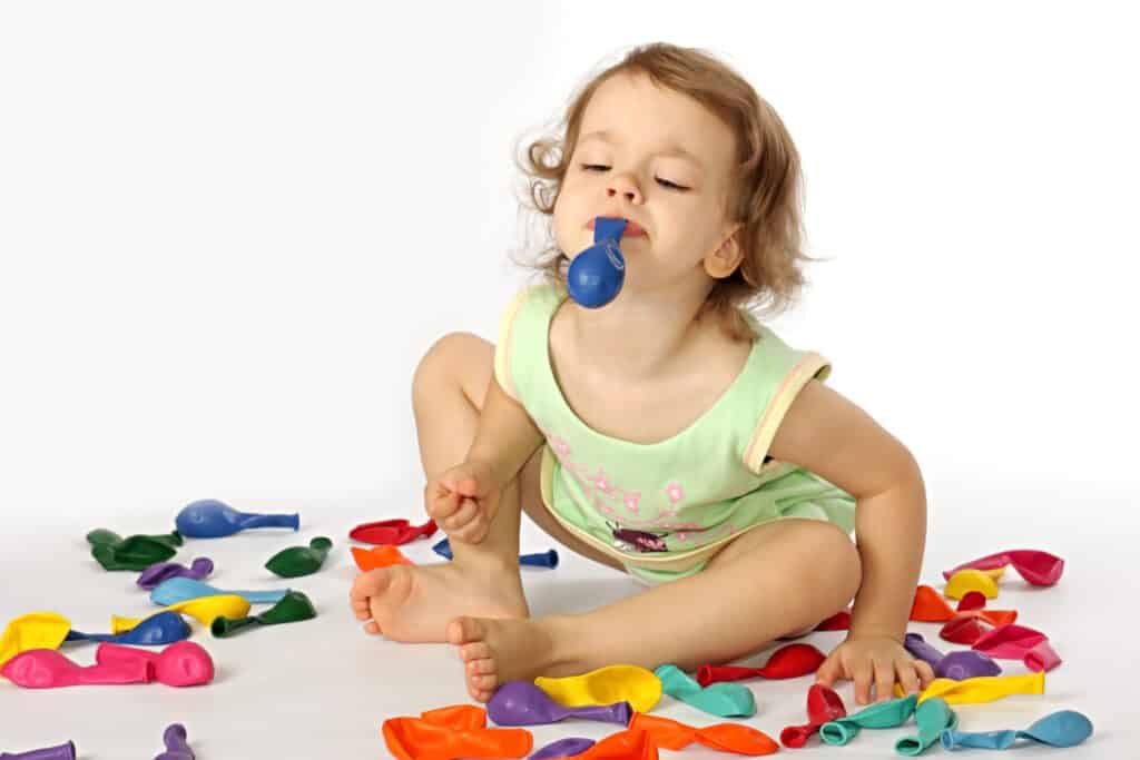 Girl with a latex balloon in her mouth with balloons around her