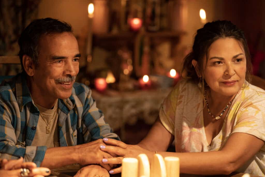 Photo showing Mexican American man and woman sitting at a table with candles in the background. They are holding hands.