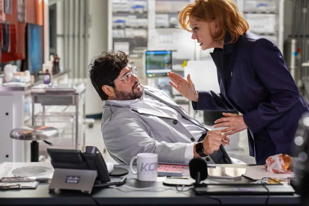 Susan Sarandon stars as Victoria Kord and Harvey Guillen as Dr. Sanchez in the Blue Beetle. Photo shows Sarandon confronting Dr. Sanchez in the laboratory.